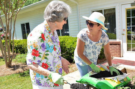 Two women engaging in gardening activities on a sunny day, showcasing teamwork and community spirit.