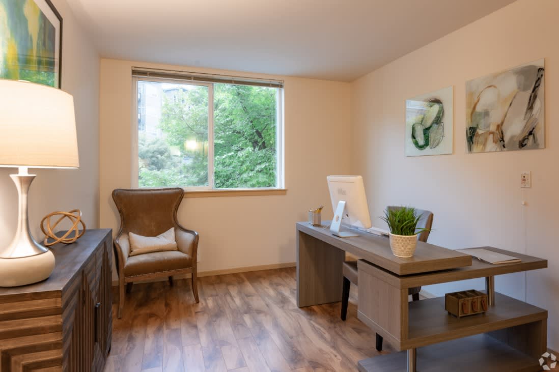 A minimalist home office with a wooden desk, chair, and a large window overlooking greenery.