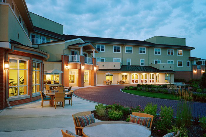 A well-lit retirement home with outdoor seating and landscaped surroundings at dusk.