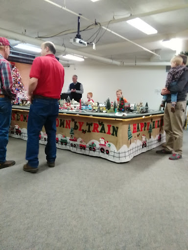 A group of hobbyists gathered around a decorated model train display at an indoor event.