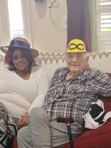 Two people sitting indoors, wearing playful hats and smiling.