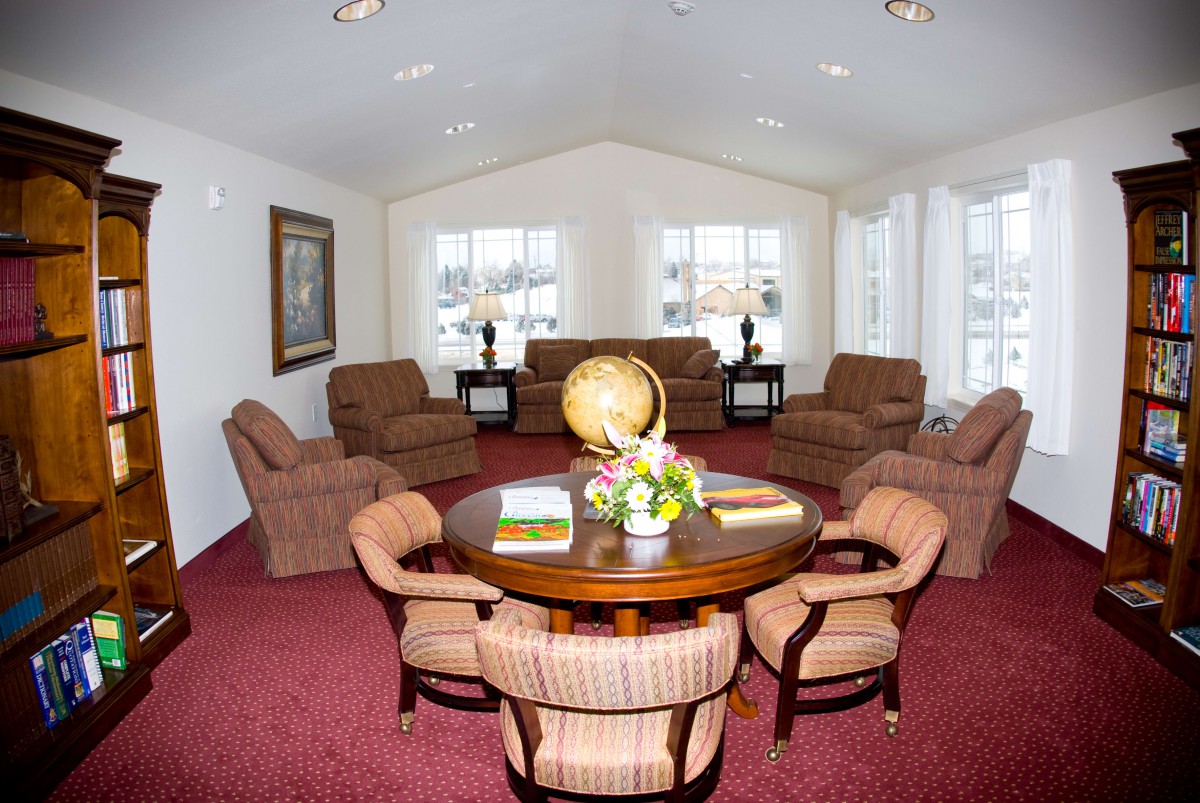 A spacious living room with a central table surrounded by chairs, featuring comfortable seating and decorative elements.