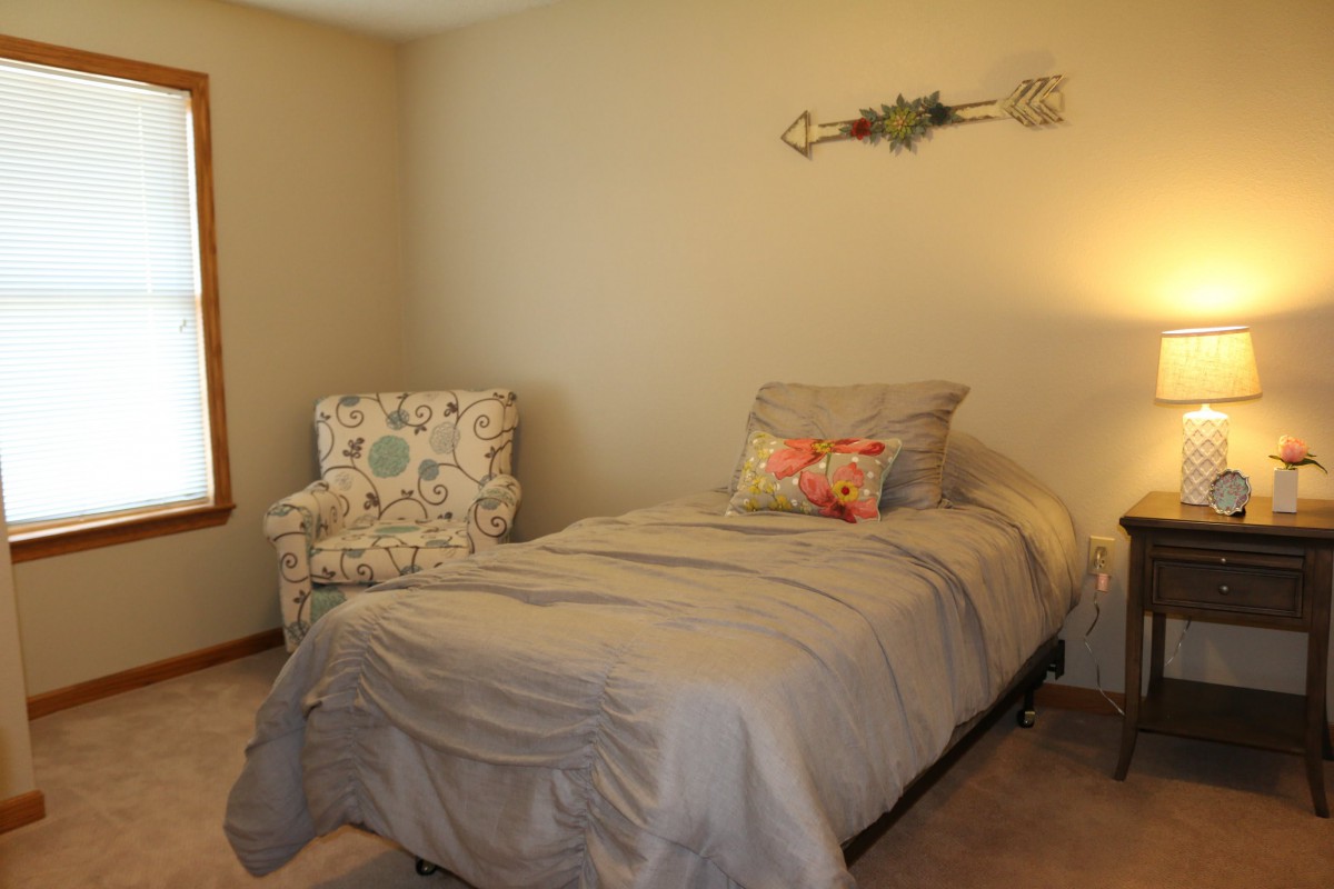 A cozy bedroom with a single bed, an armchair, and soft lighting.