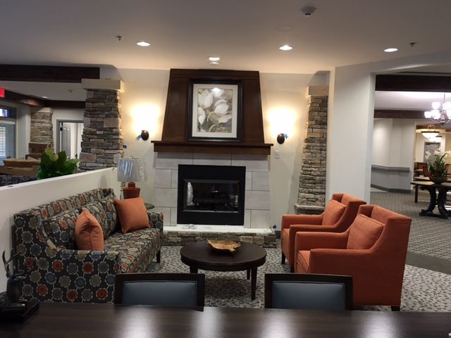 A cozy living room with a fireplace surrounded by a seating area, featuring a patterned couch and orange armchairs.