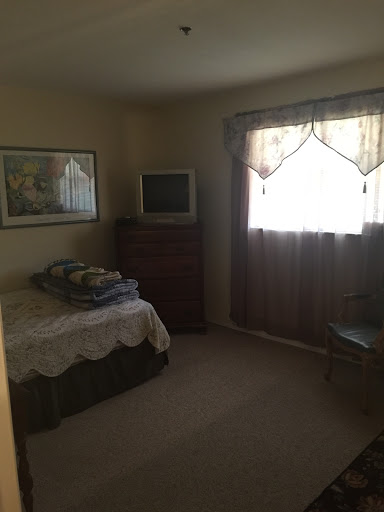 A cozy bedroom featuring a bed, dresser, and a window dressed with curtains.
