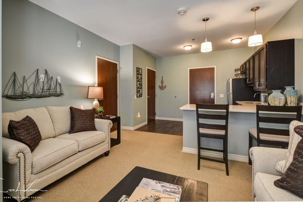 A modern apartment living room with an open concept design, featuring a comfortable sofa, kitchen counter, and stylish ceiling lights.