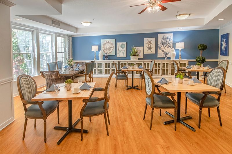 A cozy dining room with neatly arranged tables and chairs, featuring a blue accent wall and wooden flooring.