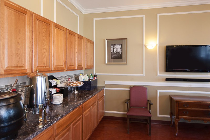 A small kitchen area with wooden cabinets, a coffee station, and a wall-mounted TV.