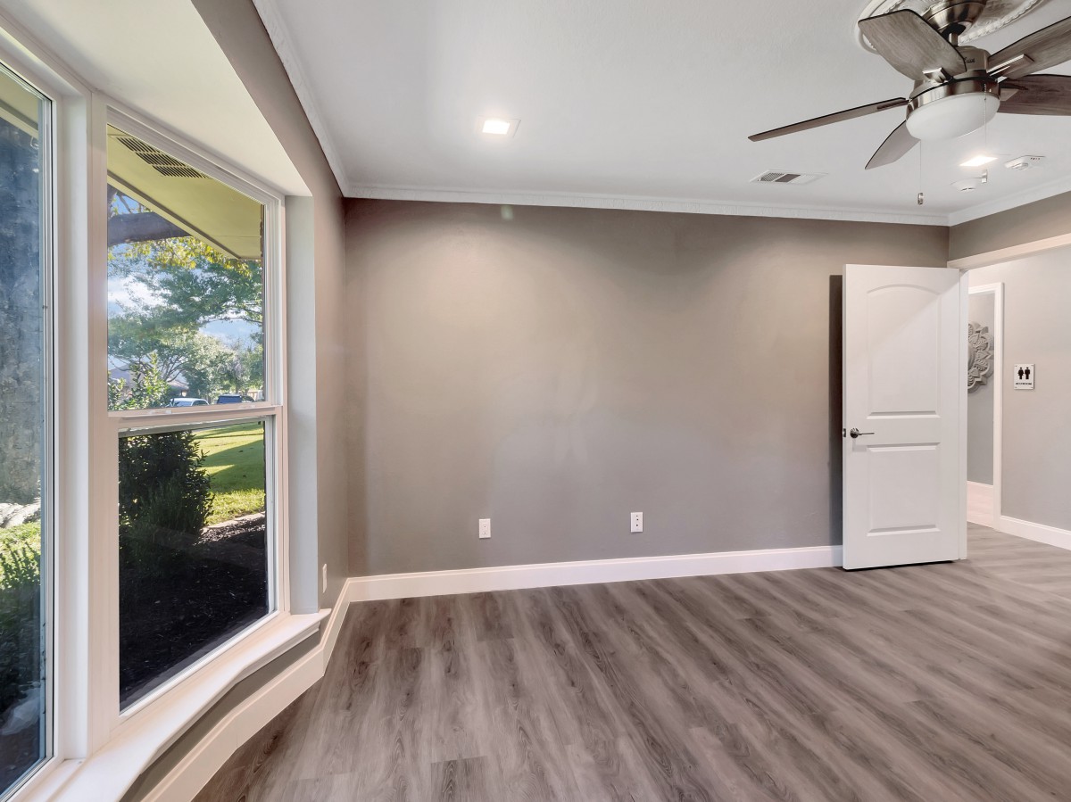 An empty room featuring wood flooring, a large window, ceiling fan, and door.
