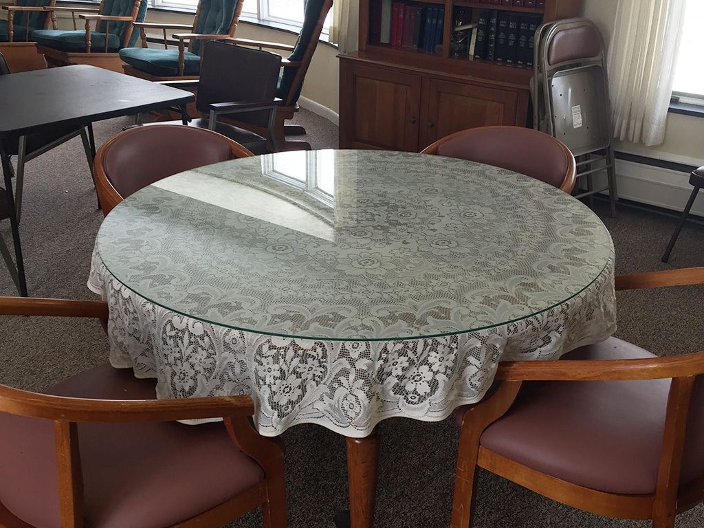 A round table with a decorative cover, surrounded by chairs in an office setting.