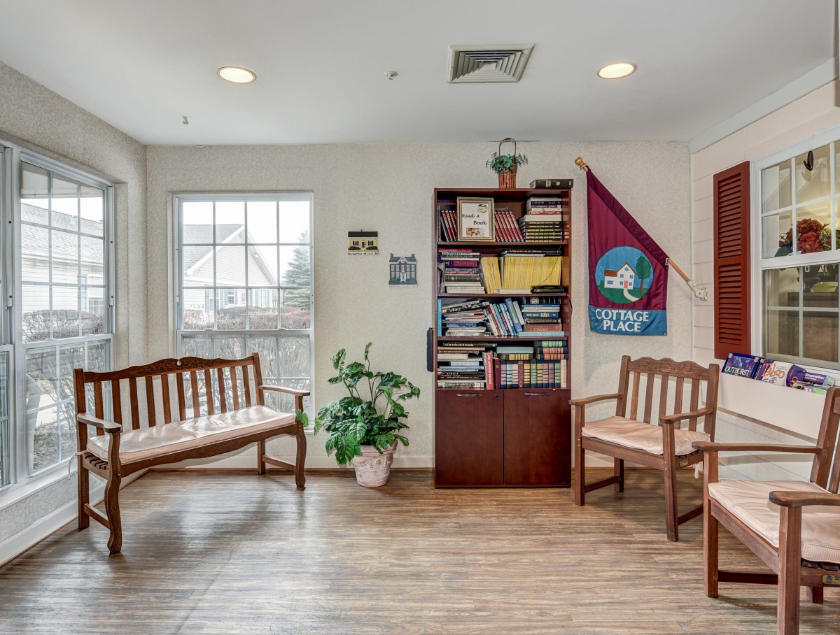 A cozy waiting room with wooden benches, a bookshelf filled with books, and a potted plant by the window.