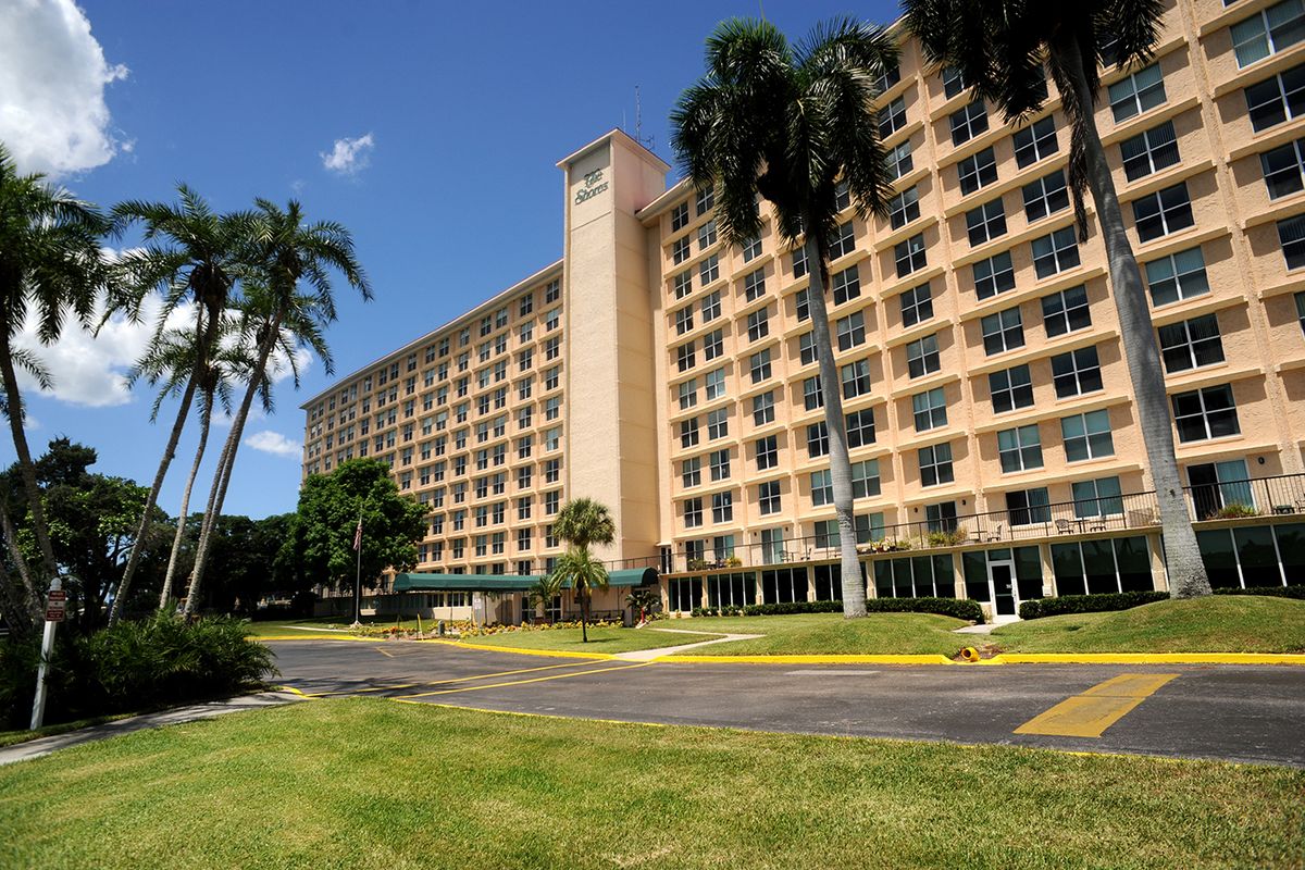 A large hotel building with palm trees surrounding it, set against a clear blue sky.