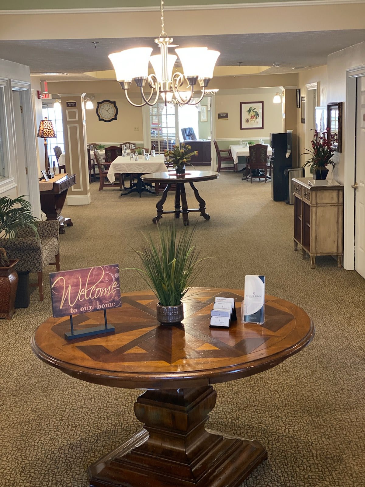 A well-decorated lobby with a central wooden table adorned with plants and brochures, leading to an open reception area.
