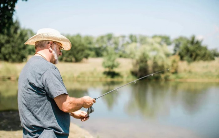 A person wearing a hat is fishing by a calm lake.