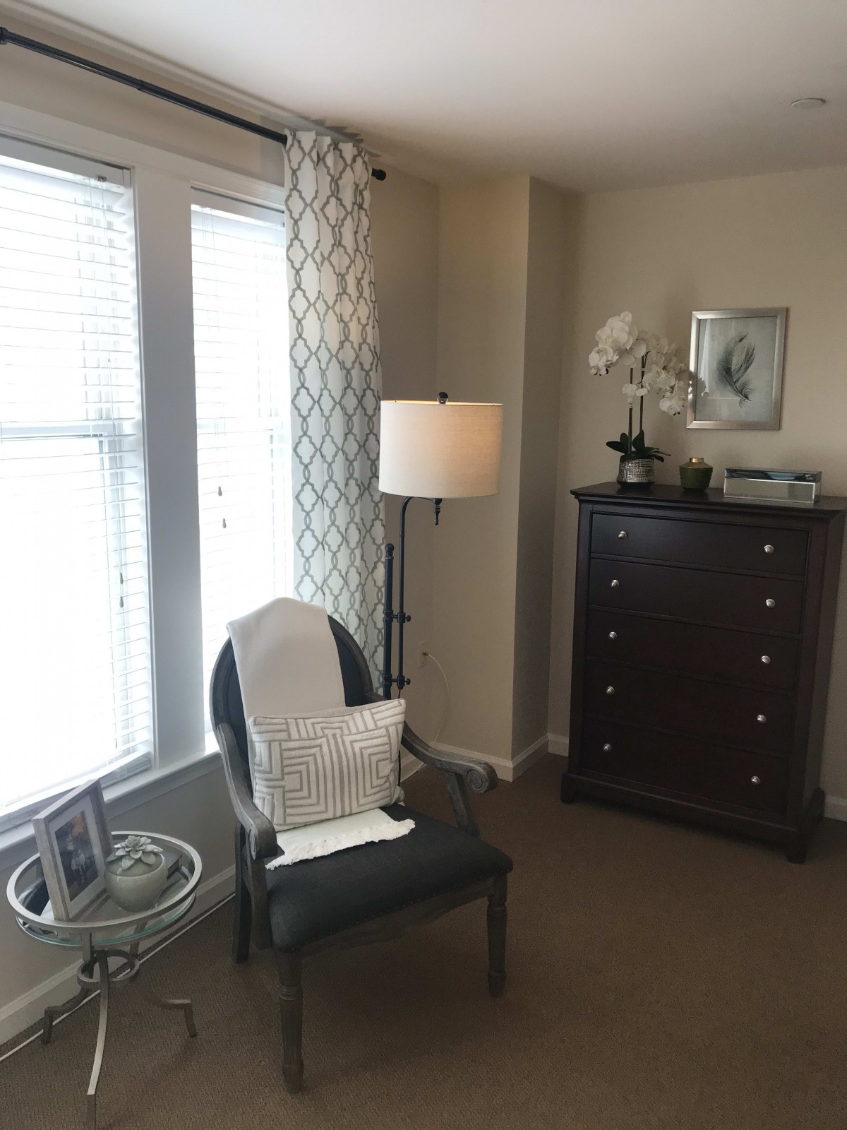 A cozy corner of a living room featuring a chair, lamp, and dresser.