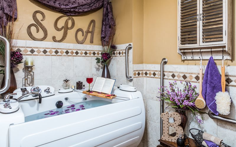 A cozy spa setting with a bathtub, candles, a glass of wine, an open book, and lavender accents creating a relaxing atmosphere.
