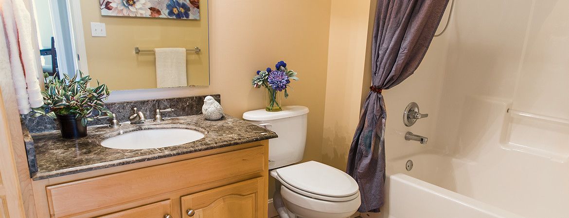 A cozy bathroom with a granite countertop, decorated with a vase of flowers on the toilet tank and an elegant curtain.