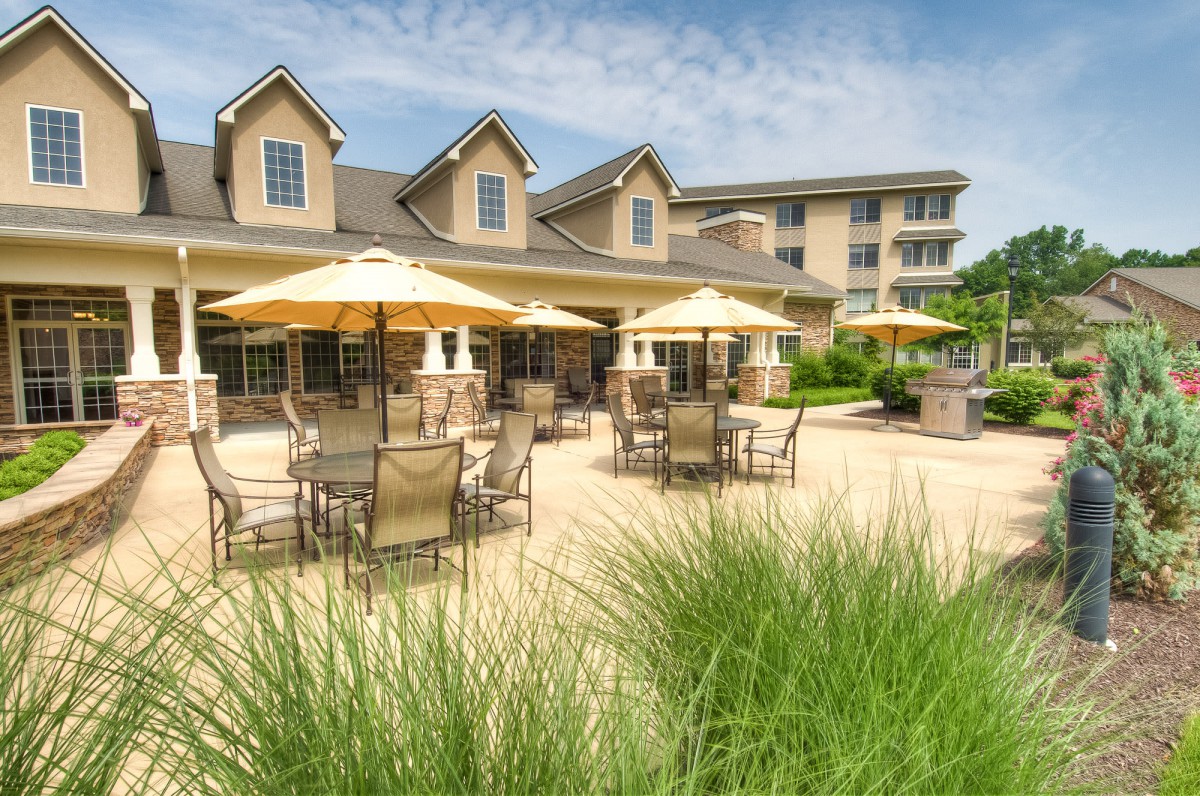 A sunny outdoor patio area with tables and umbrellas in front of a residential building.