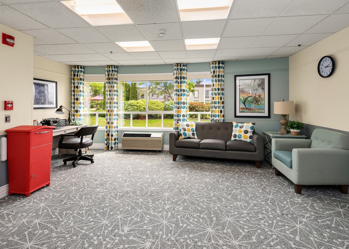 A cozy living room and office space with modern furniture, large windows, and patterned decor.
