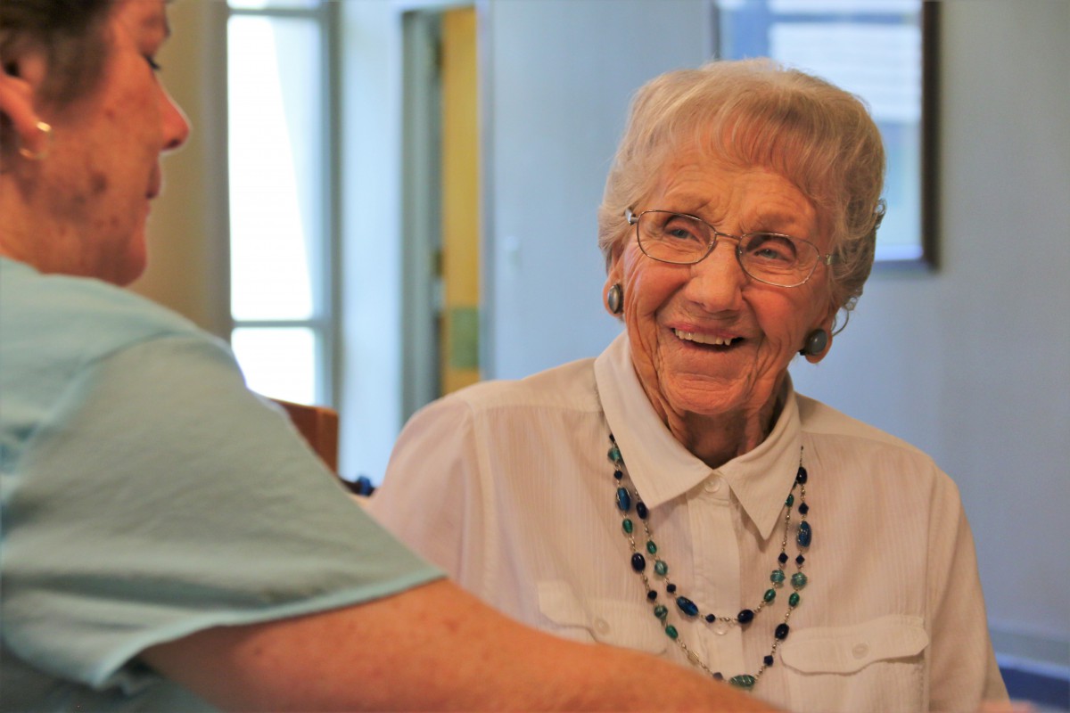 An elderly woman smiling during a conversation indoors.