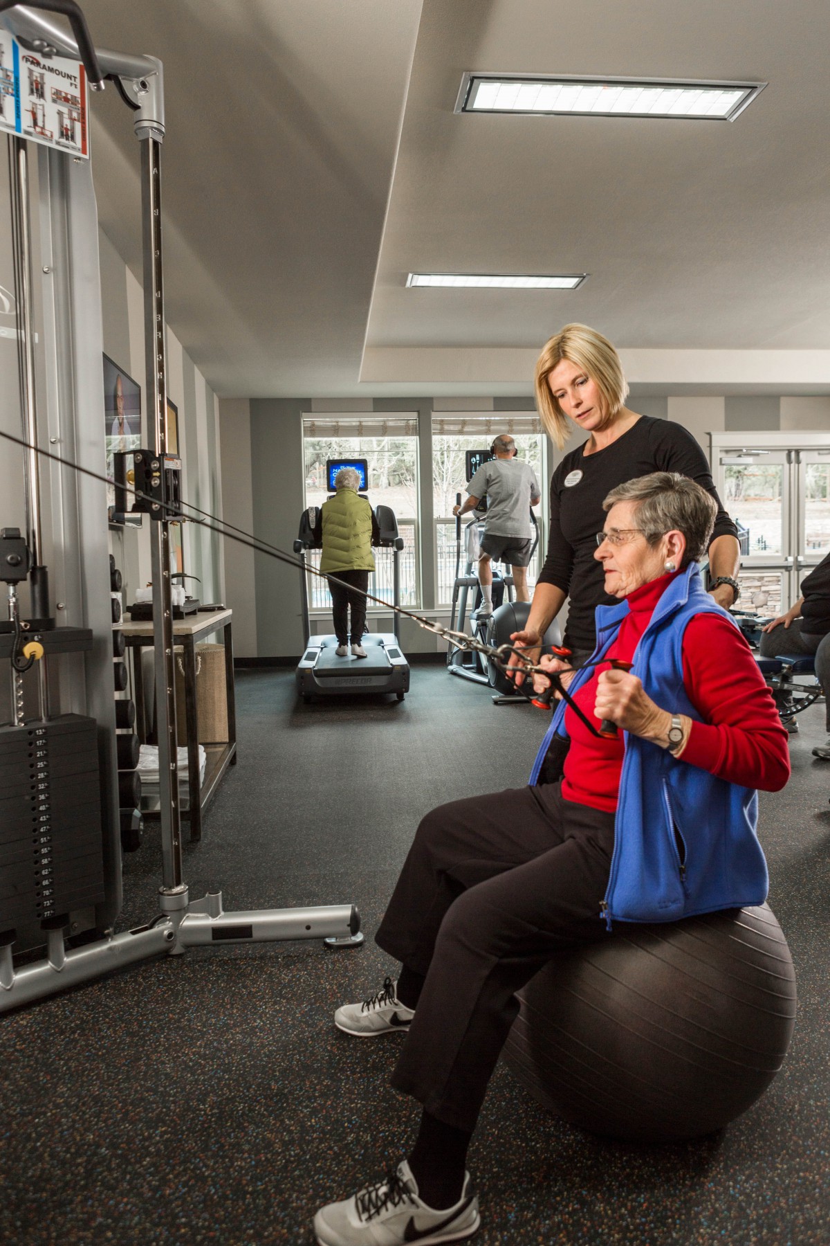 An elderly person performs resistance exercises with the guidance of a fitness trainer in a gym.