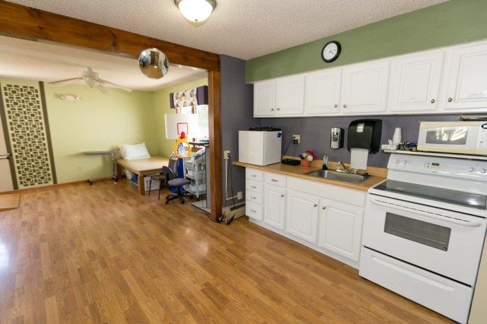 A cozy kitchen with white cabinets and a wooden floor, featuring an adjoining dining area.