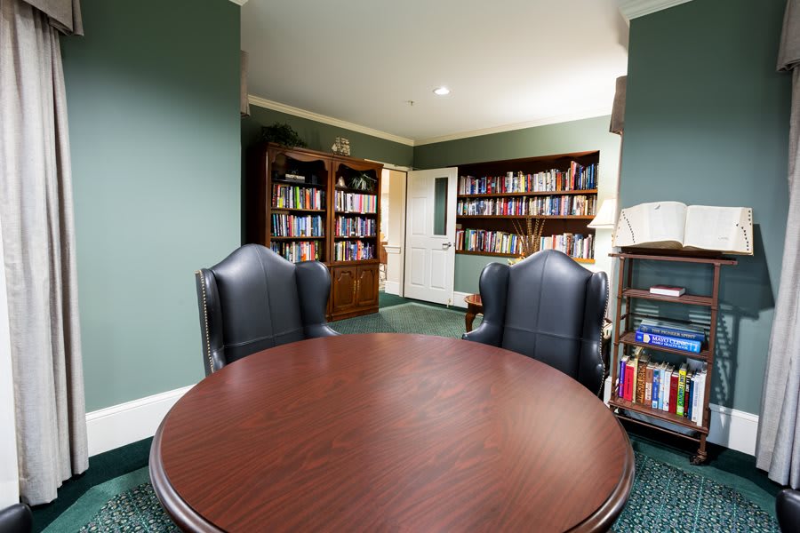 A cozy library room with a round table, leather chairs, and bookshelves filled with books.