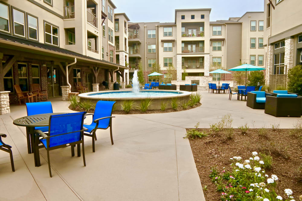 A modern apartment complex courtyard featuring a central fountain and blue outdoor seating.