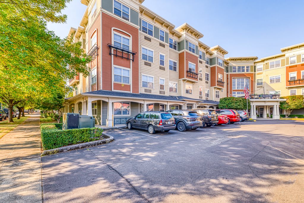A modern apartment building with a parking lot and parked cars in an urban setting.