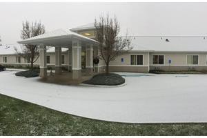 A snowy driveway leads to a building entrance surrounded by winter trees on an overcast day.