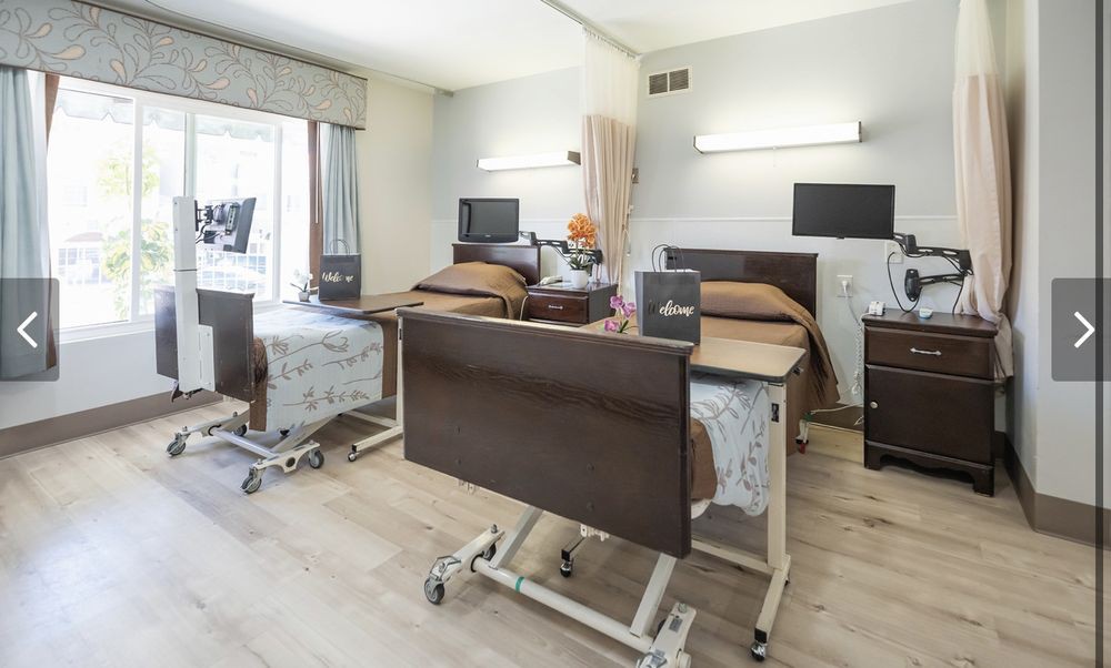 A bright and clean hospital room with two patient beds, equipped with medical furniture and amenities.