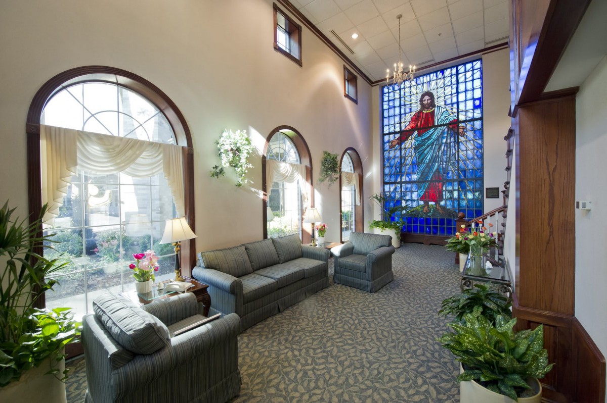 A cozy lobby area featuring comfortable sofas, large arched windows, and a vibrant stained glass artwork.