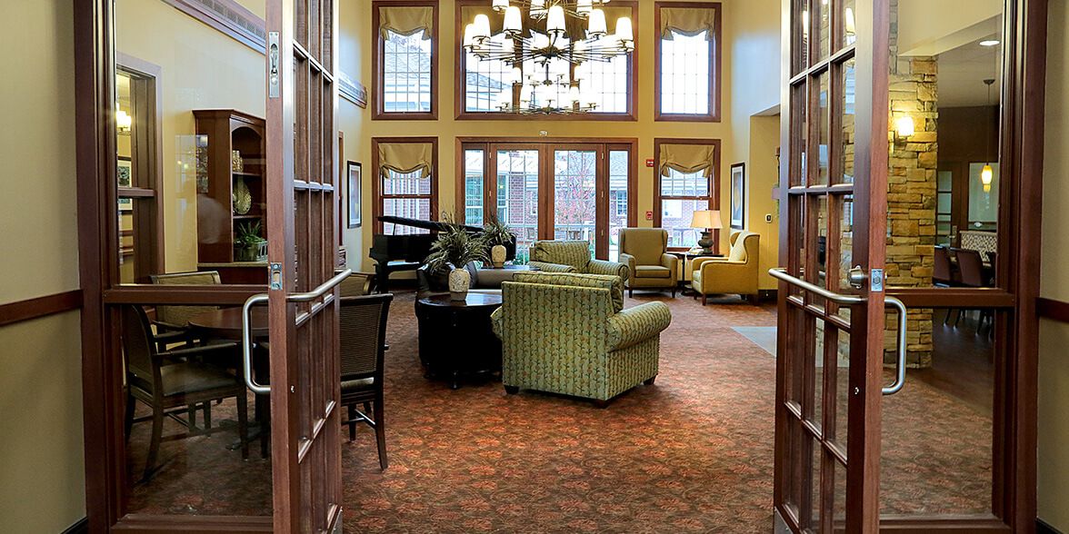 A cozy lounge area with comfortable seating, large windows, a grand piano, and an elegant chandelier.