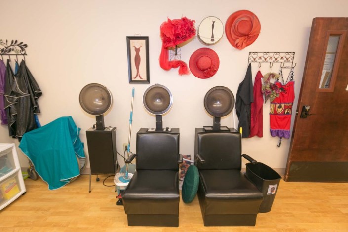 A cozy hair salon interior featuring black chairs with dryers, adorned walls with decorative hats, and vibrant red accents.