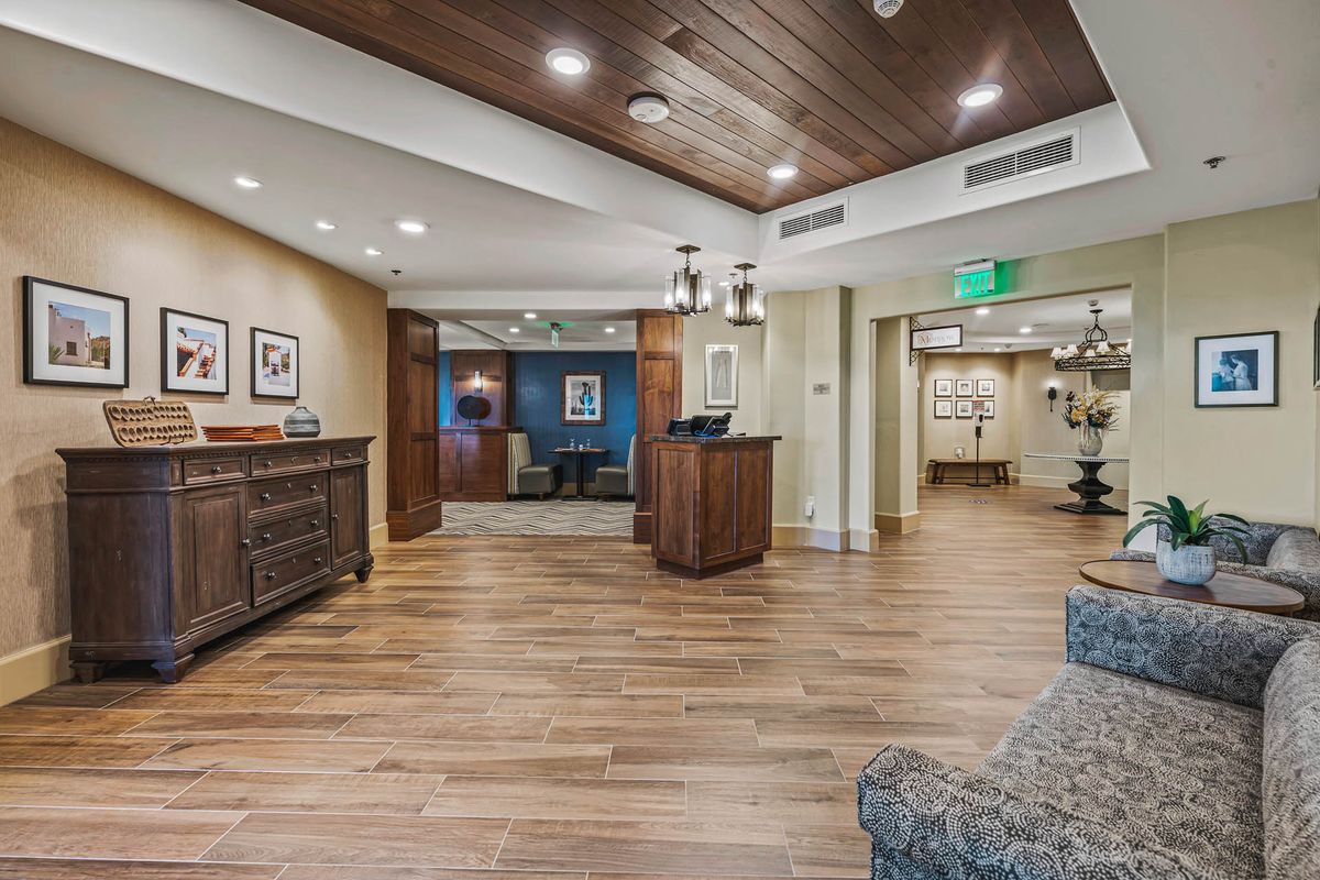 A spacious lobby area with a wooden floor, featuring a reception desk and comfortable seating.