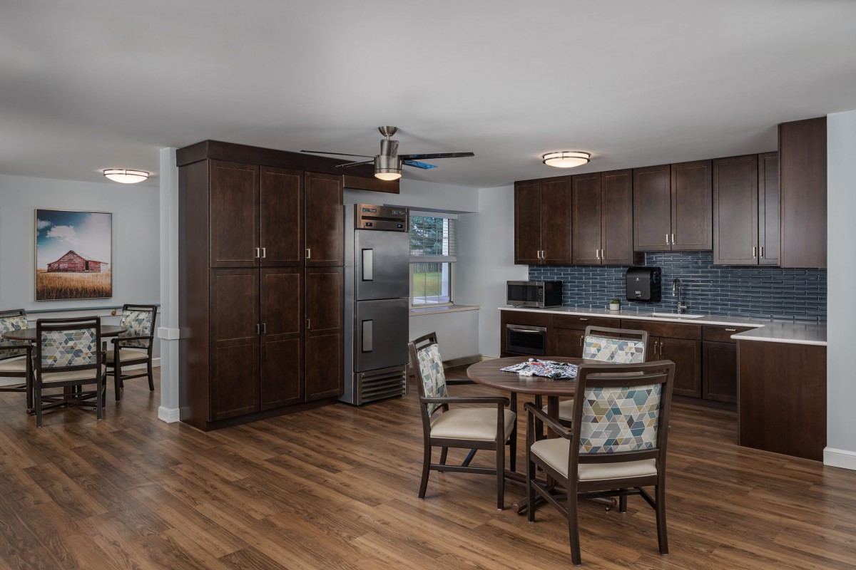 A modern kitchen and dining area featuring wooden flooring, dark cabinets, and a round dining table with chairs.