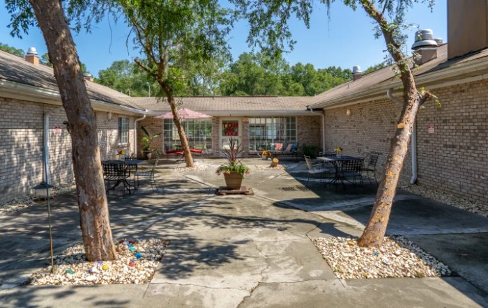 A tranquil courtyard with outdoor seating, surrounded by trees and a residential building.