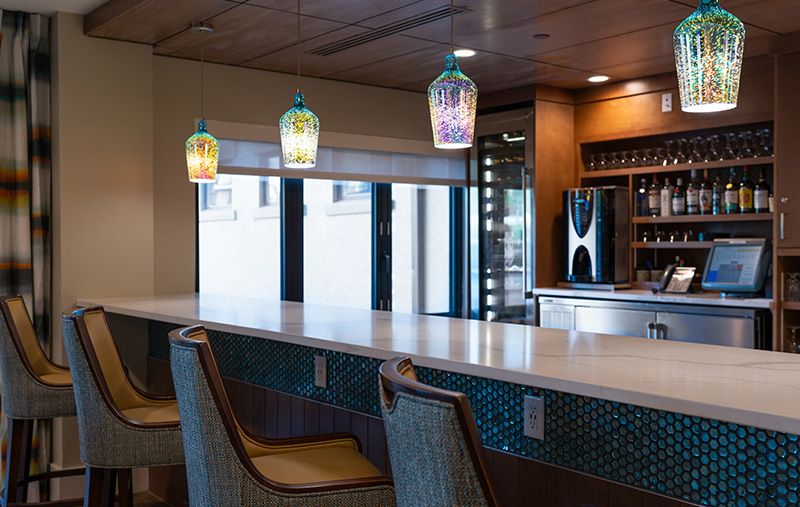 A modern bar area with colorful pendant lights and comfortable seating.