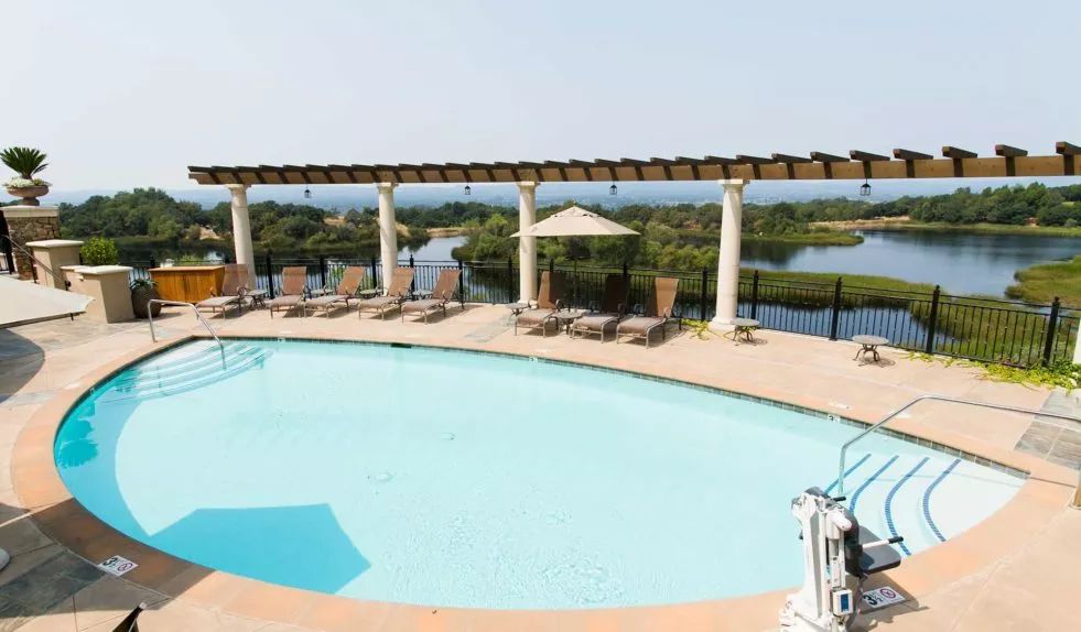 A scenic outdoor pool area with lounge chairs and a pavilion overlooking a natural landscape.
