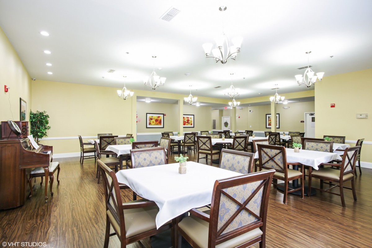 A spacious dining room with elegantly arranged tables and chairs, featuring bright lighting from chandeliers.