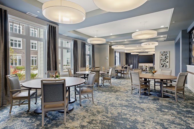 A modern conference room with round tables and chairs, featuring large lighting fixtures and a carpeted floor.
