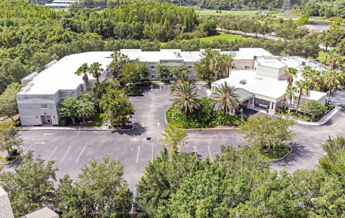 Aerial view of a building surrounded by trees and a parking lot.