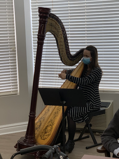 A musician playing the harp indoors while wearing a mask.