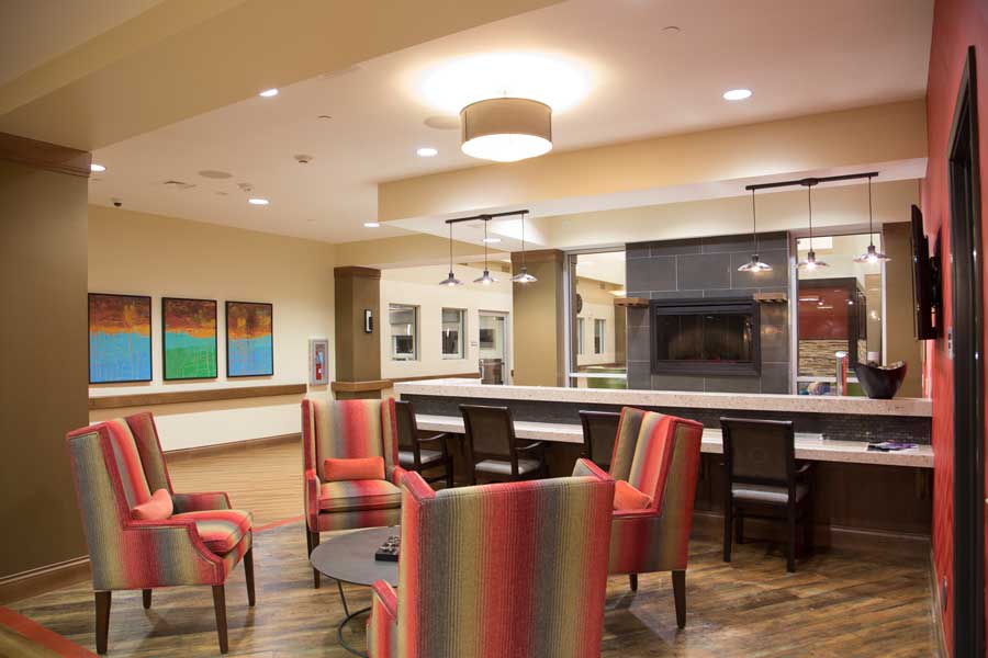 A modern lobby area featuring colorful chairs and a central fireplace.