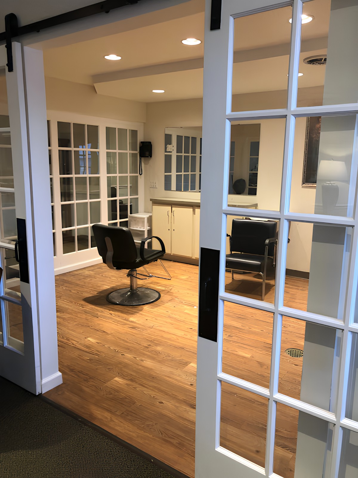 An empty room with wooden flooring, featuring chairs and glass-paneled doors.