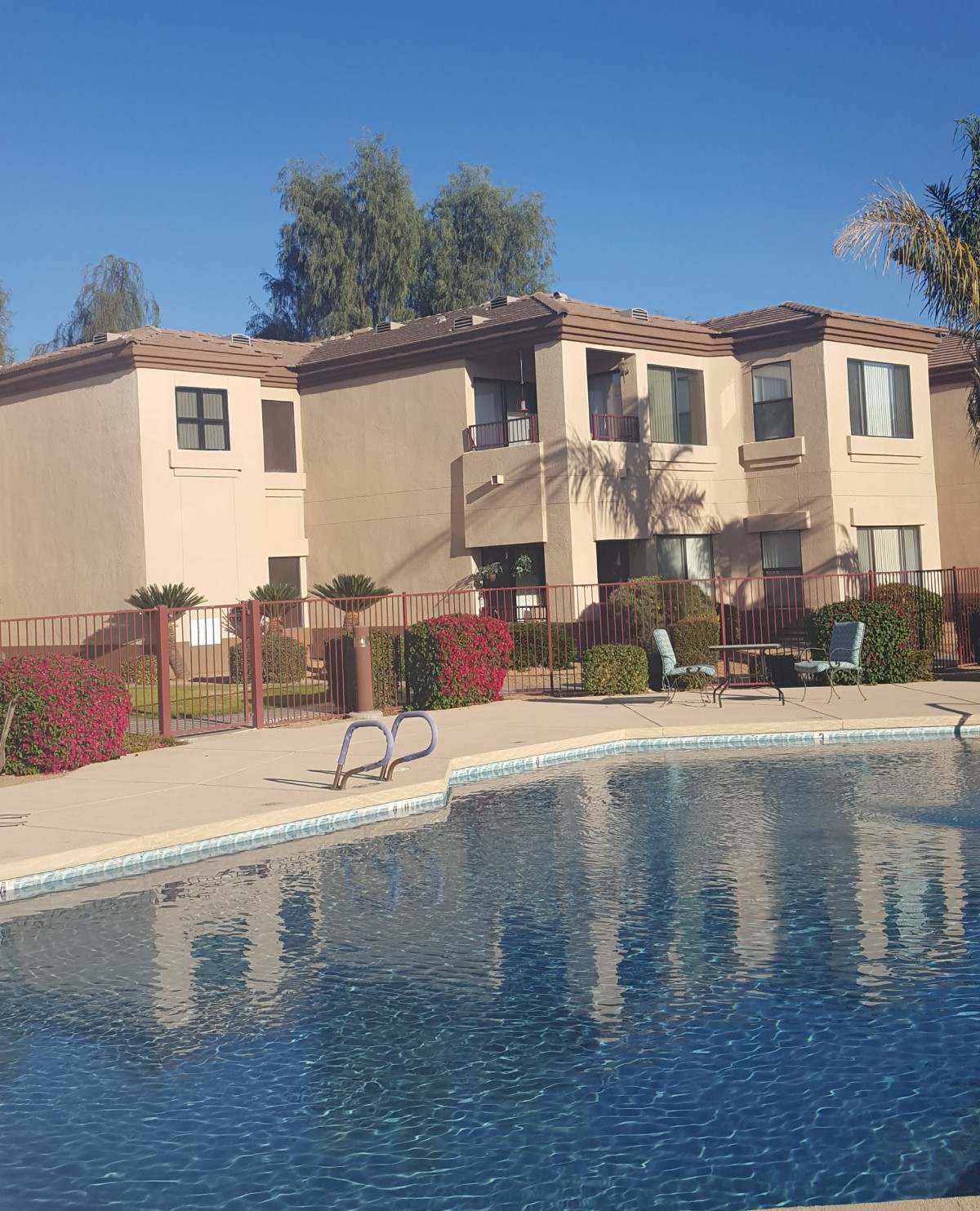 An apartment complex with a swimming pool and surrounding greenery on a sunny day.