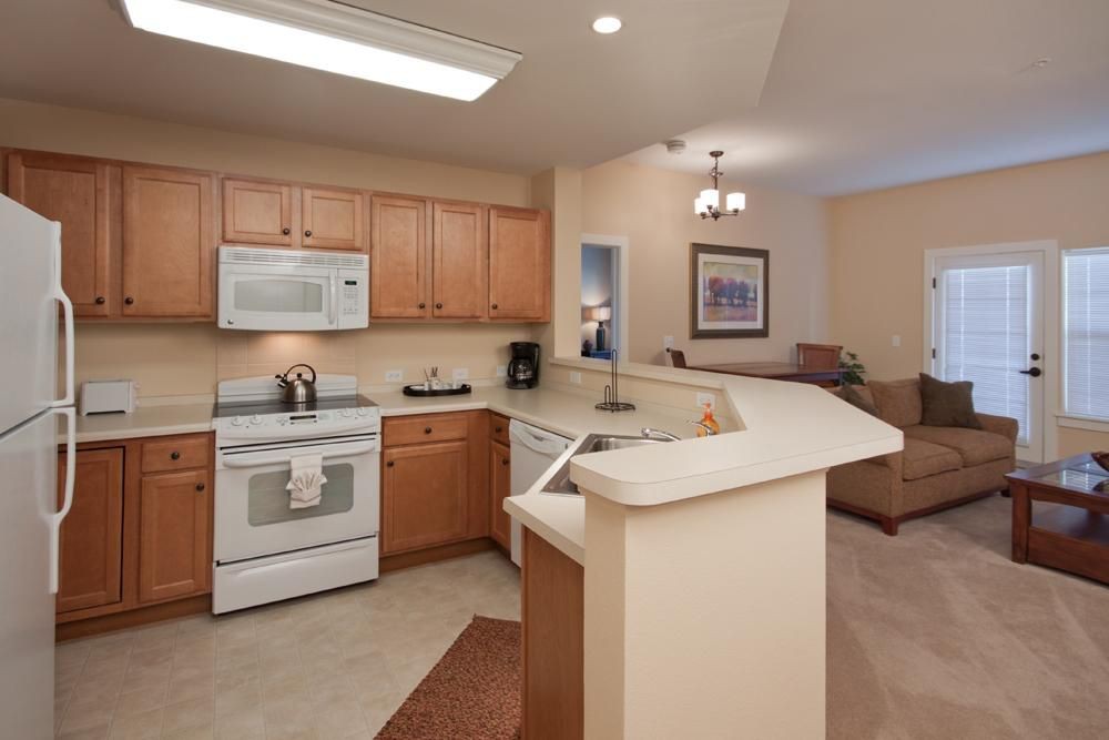 A spacious and modern kitchen featuring wooden cabinetry and white appliances, with an open layout leading to the living area.
