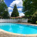 A serene outdoor swimming pool surrounded by trees and under a clear blue sky.