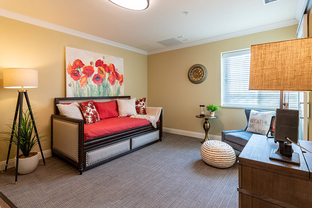 A cozy living room featuring a modern sofa with vibrant red cushions, accompanied by a floral artwork on the wall.
