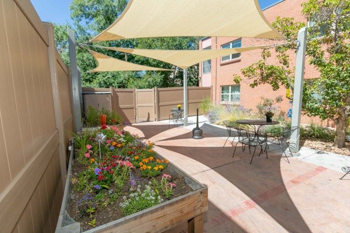 A cozy patio area with outdoor seating, shade sails, and a vibrant garden planter.